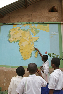 Tanzanian school children point out their country on the map of africa on the wall of their school