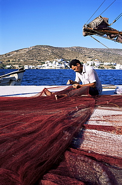 Fisherman mending nets on quayside at Katapola, island of Amorgos, Cyclades, Greece, Europe