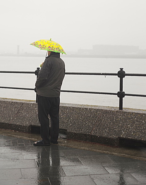 A man waits in the rain under a childs umbrella, United Kingdom, Europe