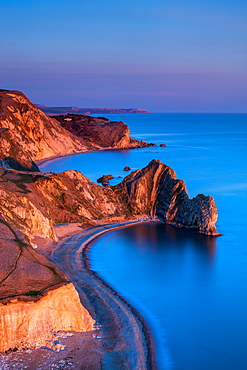 The limestone arch of Durdle Door and St. Oswald's Bay extending along the Jurassic Coast at dusk, UNESCO World Heritage Site, Dorset, England, United Kingdom, Europe