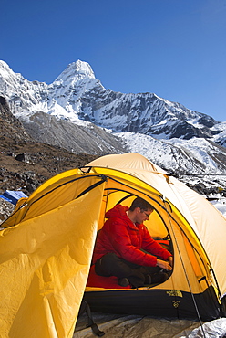 A mountaineer packs his bag in preparation to climb Ama Dablam, the 6856m peak in the distance, Khumbu Region, Himalayas, Nepal, Asia