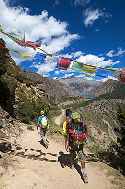 Prayer flags mark a high point in the trail where trekkers are rewarded with their first glimpse of Phoksundo Lake, Dolpa Region, Himalayas, Nepal, Asia