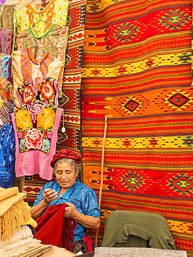 Woman sewing in market with background of handmade rugs, Oaxaca, Mexico, North America