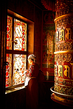 A Tibetan woman stands next to a large prayer wheel of the temple of Boudhanath Stupa, Kathmandu, Nepal, Asia