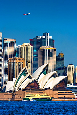 An airplane flies over the Sydney city skyline and Opera House as a ferry and water taxi pass by, Sydney, New South Wales, Australia, Pacific