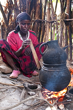 A woman blows through a wooden pipe to get the fire going whilst brewing some coffee on an open fire, Ethiopia, Africa