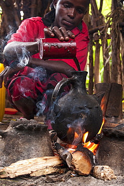 A woman pours into a traditional Ethiopian coffee pot on an open fire, Ethiopia, Africa