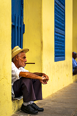 An elderly Cuban sitting on a doorstep, smoking a cigar, Trinidad, Sancti Spiritus Province, Cuba, West Indies, Caribbean, Central America