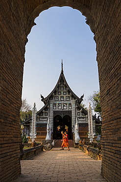 Temple Wat Lok Moli seen through an arch with two monks walking by, Chiang Mai, Thailand, Southeast Asia, Asia