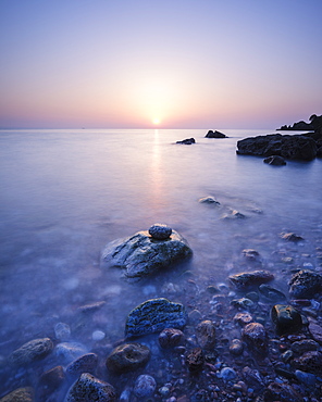 A colourful spring sunrise over Torbay with warm light glinting off the wet rocks, Anstey's Cove, Torquay, Devon, England, United Kingdom, Europe