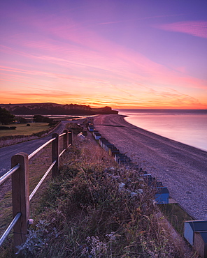 Colourful dawn with sweep of the shoreline, beach huts, pebbles and the cliff of Otter Head at Budleigh Salterton, Devon, England, United Kingdom, Europe