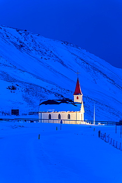 Floodlit church at dawn against snow covered mountains, winter, near Vik, South Iceland, Iceland, Polar Regions