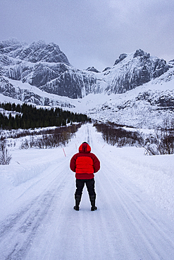 Male on snow covered road in Arctic winter conditions with mountain back drop, Lofoten, Nordland, Arctic, Norway, Europe