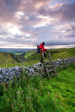 A walker climbing a stile at Winnats Pass, Winnats Pass, Hope Valley, Peak District, Derbyshire, England, United Kingdom, Europe