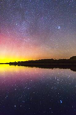 The rising autumn stars and constellations over and reflected in the lake at Police Outpost Provincial Park, in southern Alberta, on September 26, 2016. The stars of Auriga and Taurus are rising, including the Pleiades at upper right. Capella is the bright star above right centre; Aldebaran is below right in the sky. Both are reflected in the still water, along with the Hyades and Pleiades star clusters. A mild aurora is at left.