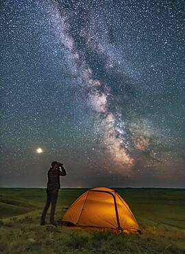 A Park interpreter poses for a scene in Grasslands National Park, Saskatchewan, of stargazing with binoculars under the Milky Way on a dark moonless night. Grasslands is perfect for stargazing as it is a Dark Sky Preserve and the horizon is vast and unobstructed.