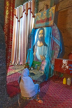 A woman sits in front of a painting of jesus Christ inside the church of Bet Medhane Alem (Church of the World Savior) in Lalibela, Ethiopia