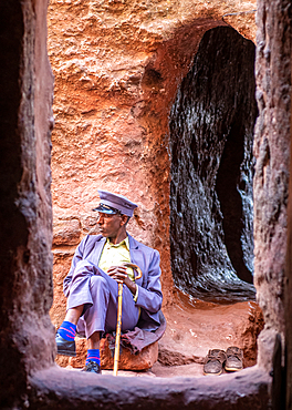 A man in a suit sits outside the rock hewn monolithic church of Bet Golgotha (House of Golgotha Mikael), known for its arts and said to contain the tomb of King Lalibela) in Lalibela, Ethiopia