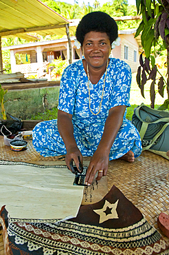 Fijian woman painting design on tapa cloth; Tongo village, Qamea Island, Fiji.