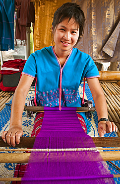 Young woman weaving cloth on loom; Patara Elephant Farm, Chiang Mai Province, Thailand.