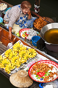 Woman selling food from boat at Damnoen Saduak Floating Market in Ratchaburi, Thailand.