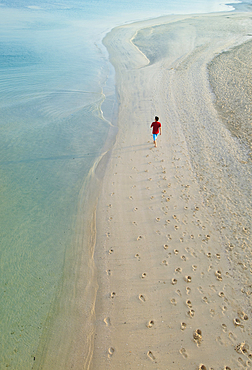 Man walking on beach next to Burj Al Arab Hotel, Dubai, United Arab Emirates.