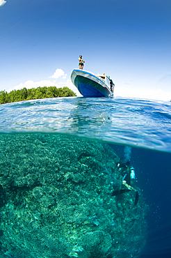 Split shot or over under of a shallow reef with a variety of table, leather, and staghorn corals, Acropora sp., Porites sp., Litophyton sp., sarcophyton sp., and the island of Bunaken, Bunaken Marine Park, Manado, North Sulawesi, Indonesia, Pacific Ocean