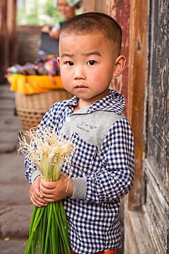 A small Chinese boy holds a bundle of green onions in the ancient town of Fenghuang, China.