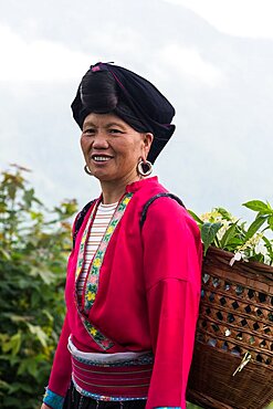 A woman of the Red Yao ethnic minority carries a basket of flowers in the Ping'an rice terraces, China.