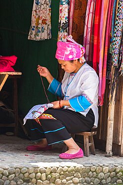 A Zhuang ethnic minority woman in traditional attire does needlework in the village of Huangluo, China.