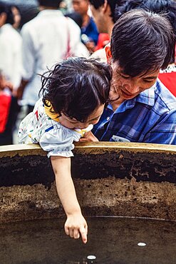 A little girl and her father reaches for a floating coin in a cistern at the Summer Palace in Beijing, China.