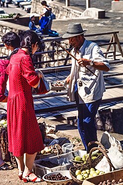 A vendor weighing produce with a hand balance scale in the farmers market in Mutianyu, China