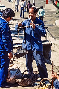 A vendor weighing produce with a hand balance scale in the farmers market in Mutianyu, China