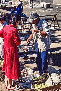 A vendor weighing produce with a hand balance scale in the farmers market in Mutianyu, China