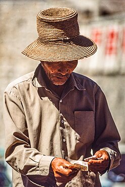 A farmer in his straw hat counts his money in an outdoor market in Mutianyu, China.