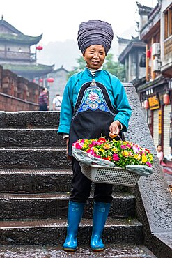 A woman in the traditional attire of the Tujia ethnic minority selling flowers in Fenghuang, China.