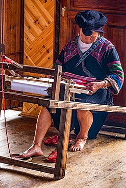 A Red Yao ethnic minority woman in traditional dress weaving fabric on a loom in Jinkeng, Longshen, China.