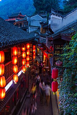 A long exposure of people walking down a narrow street in Fenghuang, China at night.