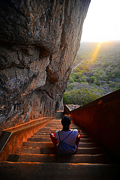 Young woman sits in lotus pose in the stairs up to the Ancient City of Sigiriya, Sri Lanka