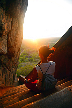 Young woman sits in lotus pose in the stairs up to the Ancient City of Sigiriya, Sri Lanka