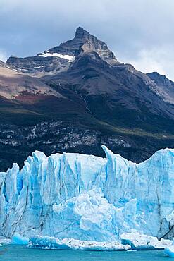 The jagged face of Perito Moreno Glacier and Lago Argentino in Los Glaciares National Park near El Calafate, Argentina.  A UNESCO World Heritage Site in the Patagonia region of South America.  Icebergs from calving ice from the glacier float in the lake.  Behind is the peak of Cerro Moreno with waterfalls on its face.