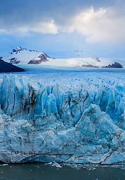 The jagged face of Perito Moreno Glacier and Lago Argentino in Los Glaciares National Park near El Calafate, Argentina.  A UNESCO World Heritage Site in the Patagonia region of South America.  Icebergs from calving ice from the glacier float in the lake.  In the distance is Cerro Gardener.