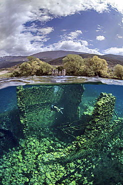 A split shot of diver taken from Capodacqua lake, in Abruzzo (Italy). Half dome is in the water depicting the submerged ruins of the middle-age mills, the other half is above water surface, showing the ancient paint factory located on the shore of the lake and, further away, the scenery of the mountains of the Tirino Valley.