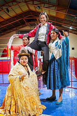 Lucha Libre. After the show. A follower is photographed with cholitas fighters. Down Julieta,  Celia la Simpatica, and Dina with blue dress , cholitas females wrestlers ,Sports center La Ceja, El Alto, La Paz, Bolivia