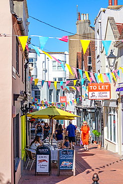 Quaint urban street with colorful bunting, outdoor cafe, and pedestrians under a clear blue sky, Brighton, Sussex, England, United Kingdom, Europe