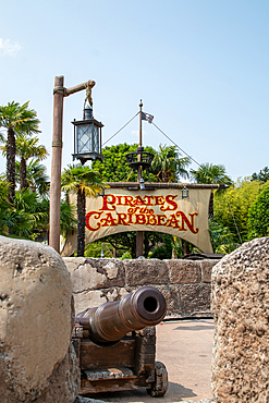 View of 'Pirates of the Caribbean' ride with cannon in foreground, sign in mid-ground, foliage, and blue sky at Disneyland Paris.