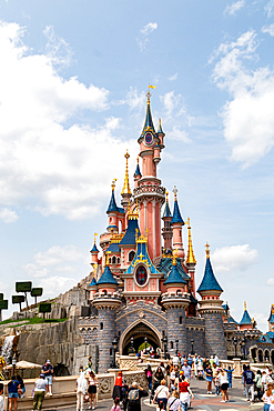 Full shot of Disneyland Paris’ castle, with a crowd of people in front and a blue sky with clouds in the background.