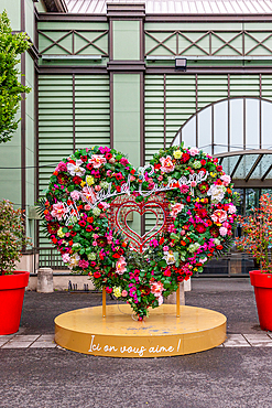 Floral heart sculpture with 'Val d'Europe' signage, standing on a gold platform with text, against a green and brown building.