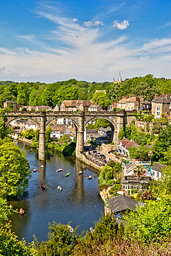 Scenic view of a stone viaduct spanning a river, with buildings, trees, and boats visible on a sunny day.