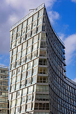 A modern, tall building with a distinctive curved facade, featuring numerous windows and balconies, set against a bright blue sky with scattered clouds in Liverpool, UK.